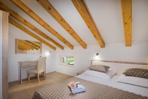 Une chambre avec un plafond en bois, un bureau avec une chaise, un lit avec des oreillers et une fenêtre.