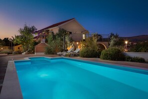 Une piscine avec des chaises longues, un bâtiment en briques avec un toit rouge et une vue sur des collines en arrière-plan.