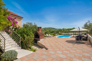 Un espace aménagé au bord de la piscine, comprenant un barbecue, des chaises longues et un escalier menant à un bâtiment.
