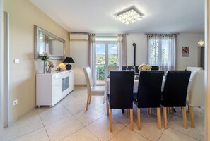 Un coin repas comprenant une table, des chaises, un meuble blanc, un miroir et une vue à travers la porte vitrée.