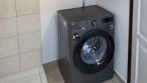 Ein kleiner Waschraum mit einer Waschmaschine, einem weißen Warmwasserbereiter und einer Steinwand.