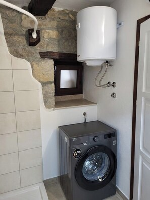 A compact laundry room with a washing machine, a white water heater, and a stone wall. - Apartment Balidur (Buzet)