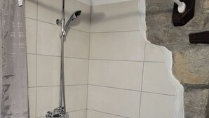 Eine Eckdusche mit Handbrause und fest installierter Duschkopf, geflieste Wände und eine Wand mit Natursteinverkleidung.
