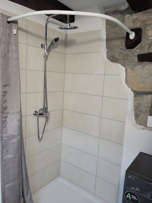 A corner shower with a handheld showerhead and a fixed showerhead, tiled walls, and a stone accent wall. - Apartment Balidur (Buzet)