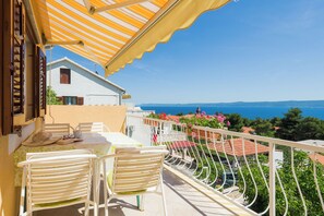 A balcony with a table and chairs, overlooking a coastal view with houses and a clear sky. - Apartments Nada (Bol)