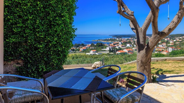 A terrace with a table and chairs, a view of the sea, and a tree. - House Dragan D (Rab)