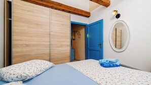 A bedroom with a bed, a wardrobe, a blue door, and a wall-mounted mirror. - House Dragan D (Rab)