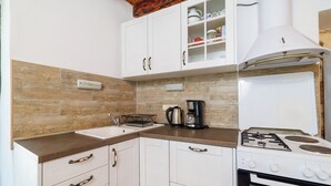 A kitchen with white cabinets, a stove, a sink, and a coffee maker. - House Dragan D (Rab)
