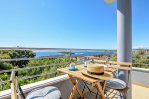 A balcony with a view of the sea, a wooden table with a straw hat, and two blue cushions. - Apartment Prcela 2 (Primosten)