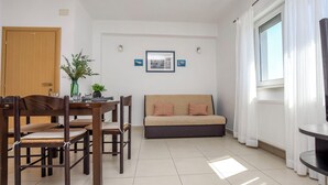 A living room with a sofa, dining table, chairs, a small plant, and a window with curtains. - Apartment Prcela 2 (Primosten)