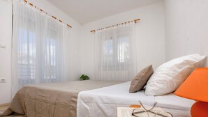 A bedroom with two beds, white bedding, a small bedside table with a book and glasses, and a plant. - Apartment Prcela 2 (Primosten)