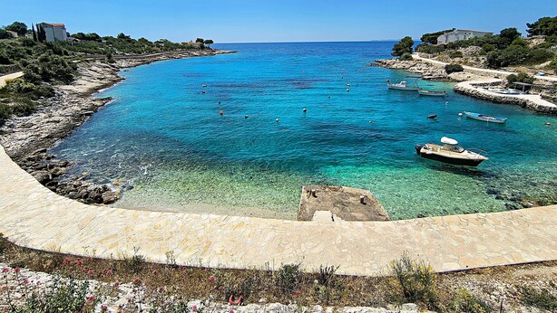 A coastal view with clear turquoise waters, boats, and rocky terrain. - Apartment Prcela 2 (Primosten)