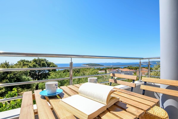 Un banc en bois, sur lequel sont posés un livre et une tasse, se trouve sur un balcon offrant une vue panoramique.