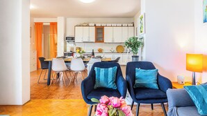 A modern living room with a dining area, featuring a sofa set, a coffee table with flowers, and a kitchen in the background. - Apartment Vito (Podgora)