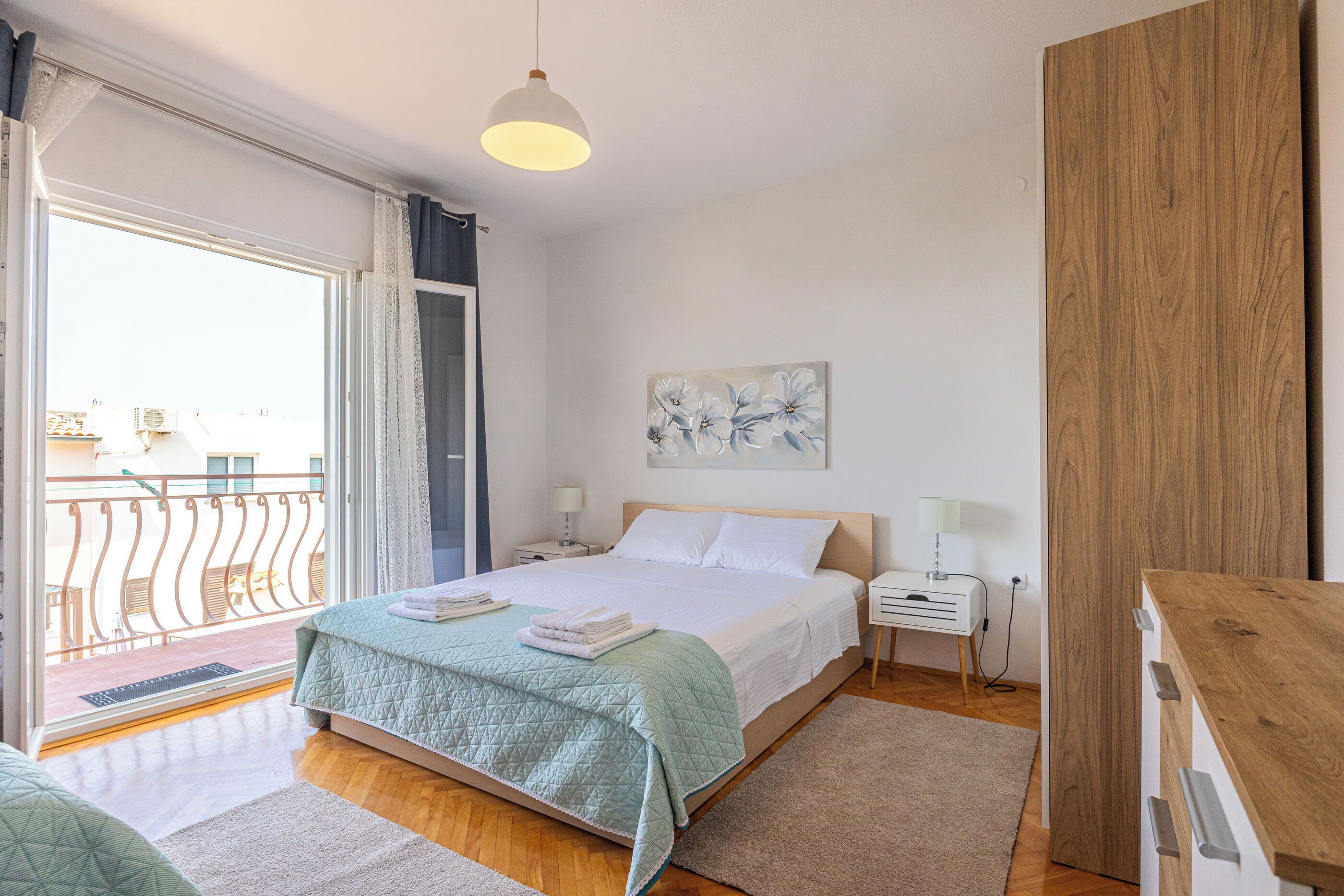 A bedroom with a bed, bedside tables, a wooden wardrobe, and a balcony with a railing.