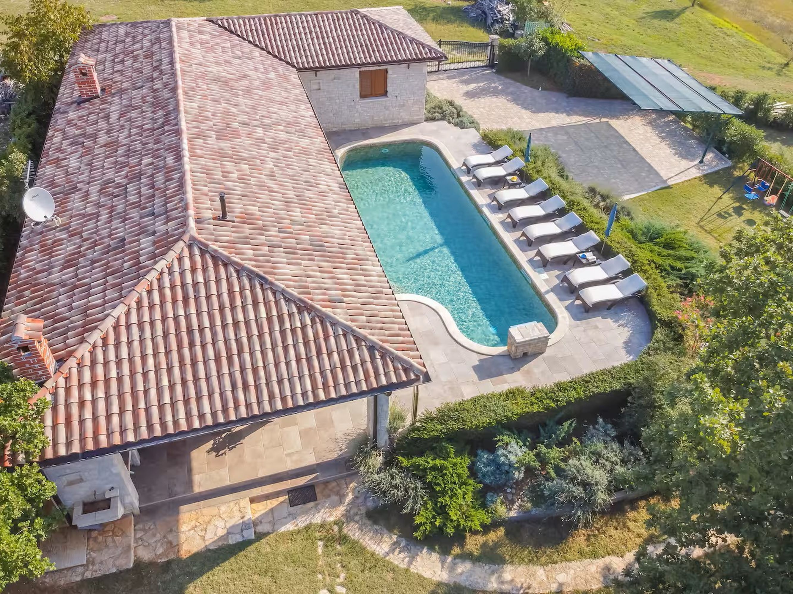 An aerial view of a house with a swimming pool, a covered patio with lounge chairs, and a solar panel array.