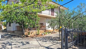 Ein zweigeschossiges Haus mit Balkon, Garten mit Kübelpflanzen und einem Metallzaun.