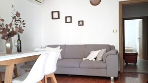 Ein modernes Wohnzimmer mit grauem Sofa, weißen Stühlen, einem Holzes Esstisch und einer Vase mit Zweigen.
