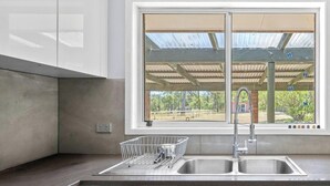 Eine Küche mit doppeltem Spülbecken, einem Fenster mit Blick auf einen überdachten Außenbereich und einem ausziehbaren Schrank.