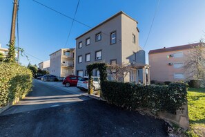A residential street with a two-story building, parked cars, and a clear blue sky. - Apartment Monika (Kastela)