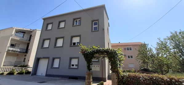 Ein mehrstöckiges Wohngebäude mit flacher Fassade, zahlreichen Fenstern und einem Balkon auf der linken Seite.