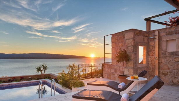A poolside area with lounge chairs, a table with drinks, and a view of the sea at sunset. - Villa Lipa Dora (Bol)