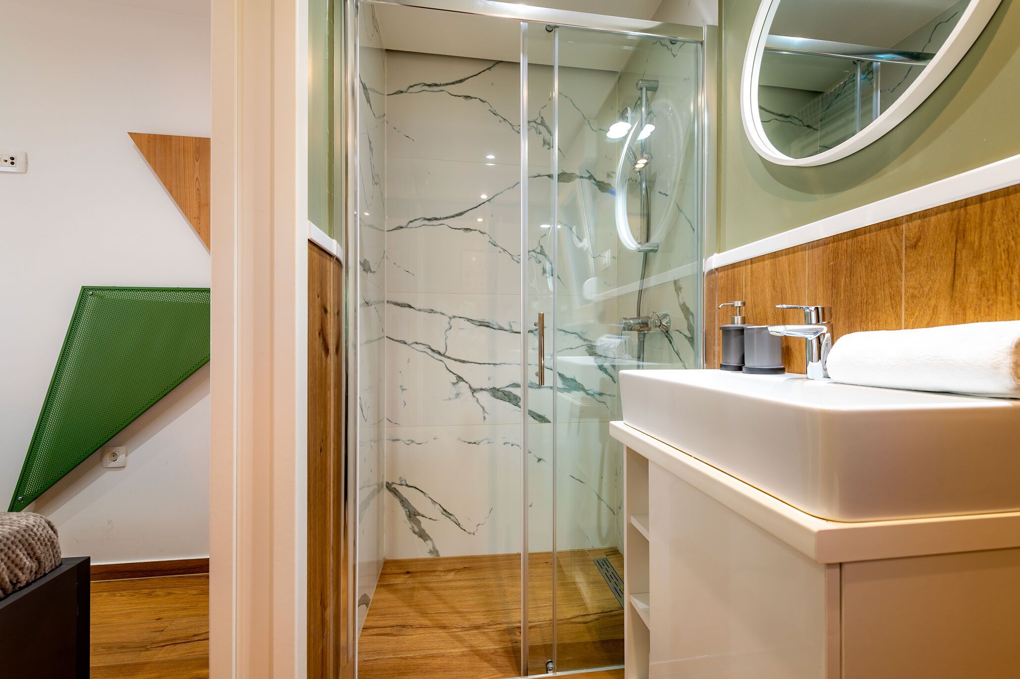 A modern bathroom with a glass-enclosed shower, a wooden floor, and a white sink with a mirror above it.