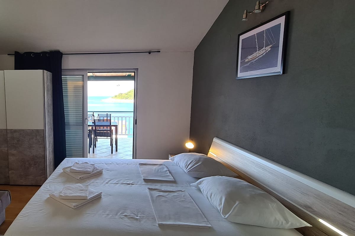 A hotel room with a bed, a sofa, a wardrobe, a TV, and a balcony with a view of the sea.