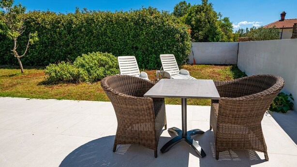 An outdoor patio with wicker furniture, including two chairs and a table, set against a backdrop of greenery and a clear sky. - House Peroj (Vodnjan)