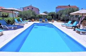 Ein rechteckiger Swimmingpool mit blauem Wasser, umgeben von Liegestühlen und Sonnenschirmen.