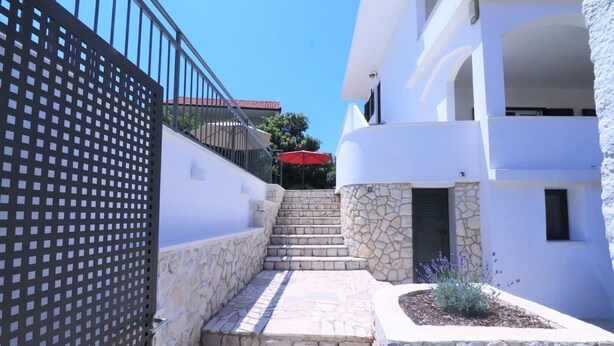 Una estrecha escalera de piedra que conduce a un edificio blanco, con un muro de piedra a un lado y una cerca de metal al otro.