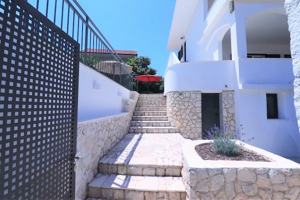 A narrow stone staircase leading to a white building with a stone wall on one side and a metal fence on the other. - House Villa Mendula (Okrug)