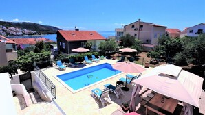 A pool area with lounge chairs and umbrellas, surrounded by buildings and a view of the sea. - House Villa Mendula (Okrug)