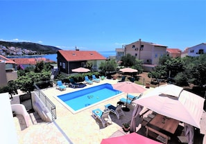 A pool area with lounge chairs and umbrellas, surrounded by buildings and a view of the sea. - House Villa Mendula (Okrug)