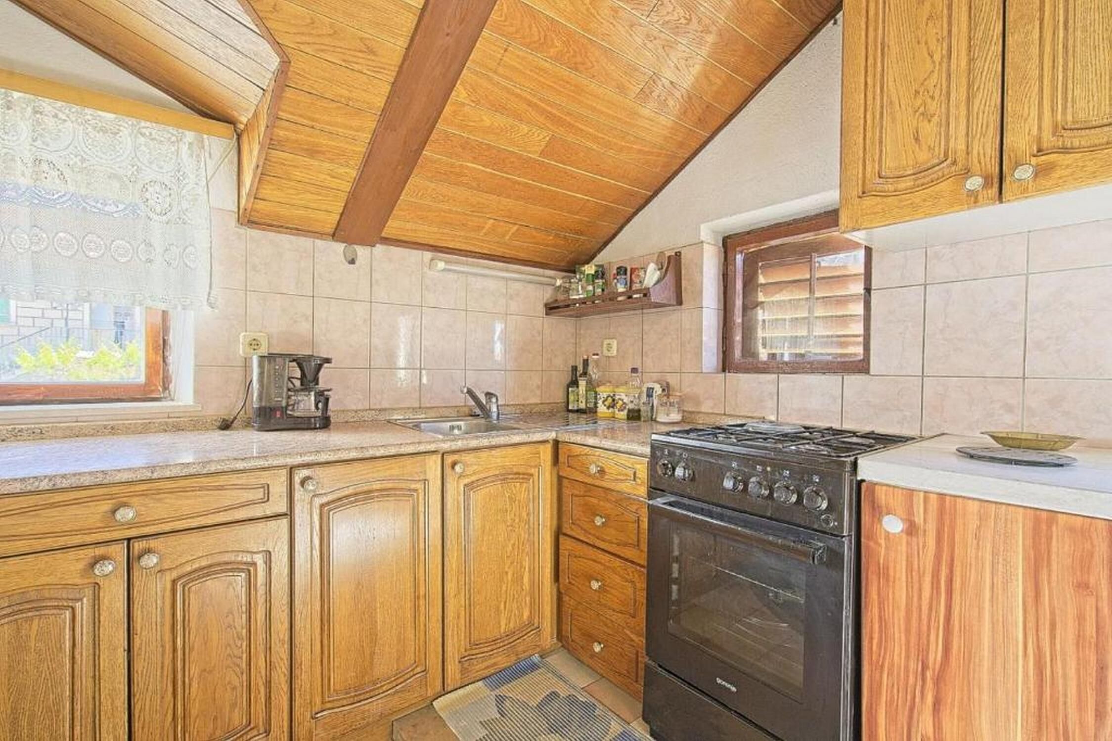 A kitchen with wooden cabinets, a stove, and a window with blinds.