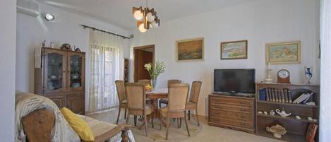 A living room with a dining table, chairs, a TV, and a bookshelf.