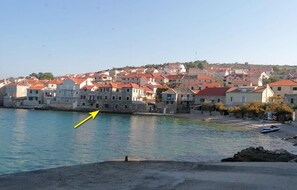 A coastal town with stone buildings and red roofs, a body of water, and a boat docked on the shore. - Apartments Lucija (Postira)