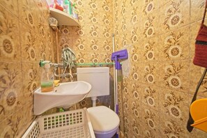 A small bathroom with floral patterned tiles, a white sink, a toilet, and a mop leaning against the wall. - Apartments Lucija (Postira)