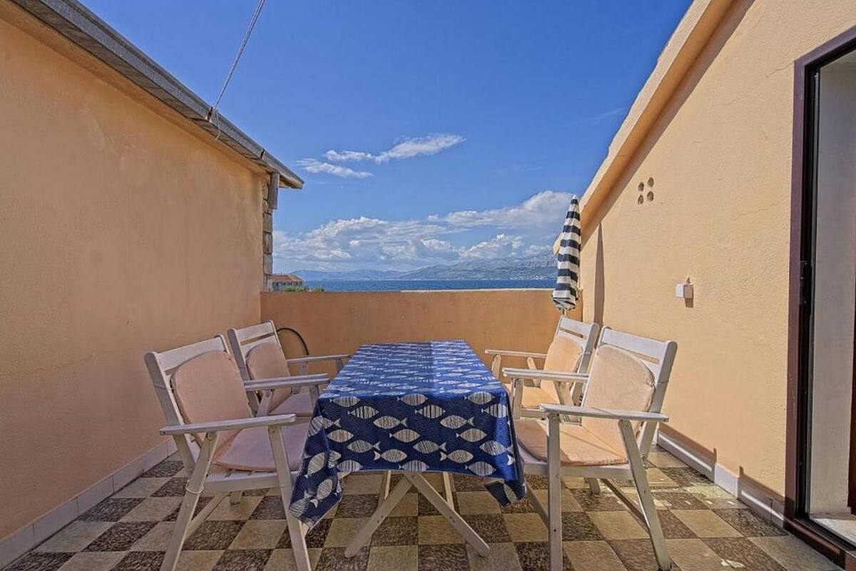 A balcony with a table and chairs, a checkered floor, and a view of the sea.