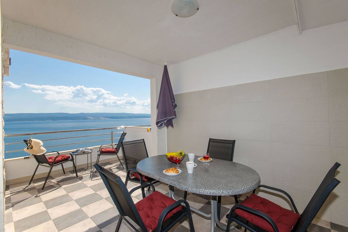 Un balcon avec une table à manger, des chaises et une vue sur la mer.