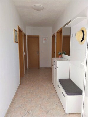 A narrow hallway with a tiled floor, wooden doors, a small bench, and a mirror with a hat hanging on the wall. - House Peacefull Relax (Jelsa)