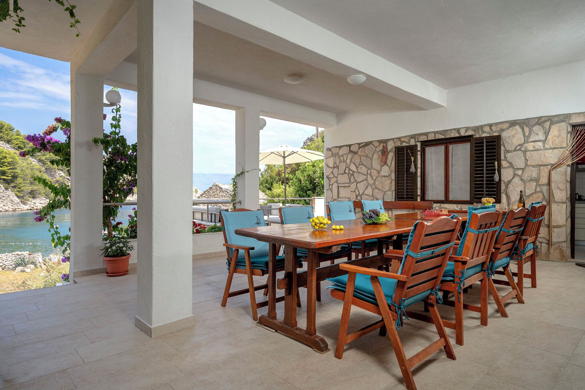 A covered outdoor dining area with a stone wall, wooden table, and chairs.
