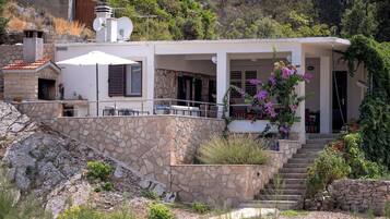 Una casa moderna con facciata in pietra, un'area salotto esterna coperta e una scala che conduce all'ingresso.