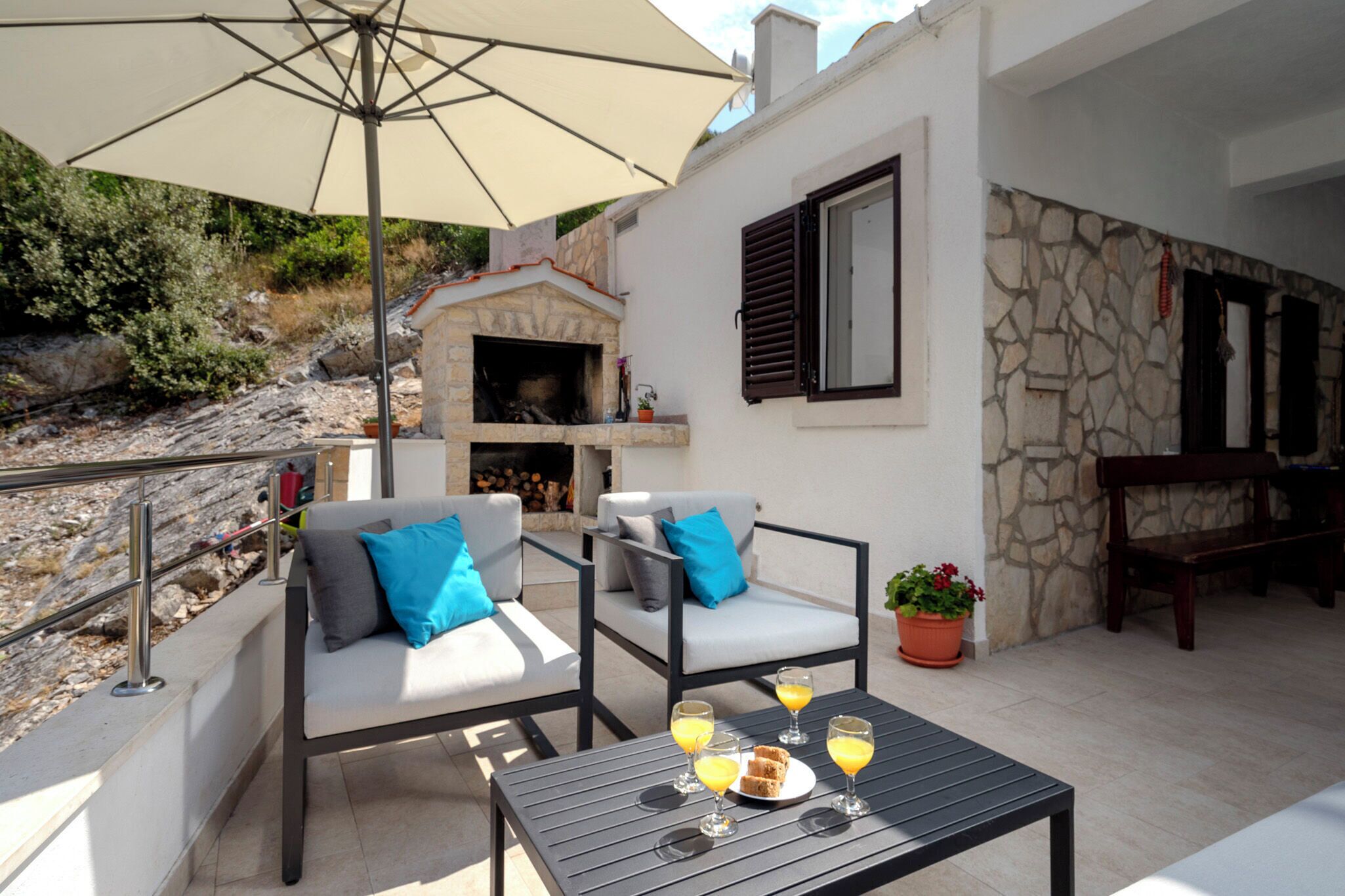 An outdoor seating area with two chairs, a table with drinks, and a stone fireplace.