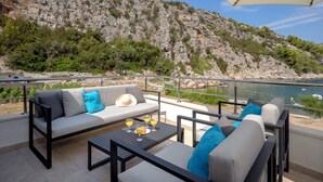 A terrace with a sofa, chairs, and a table with drinks, overlooking a rocky coastline and a body of water. - House Peacefull Relax (Jelsa)