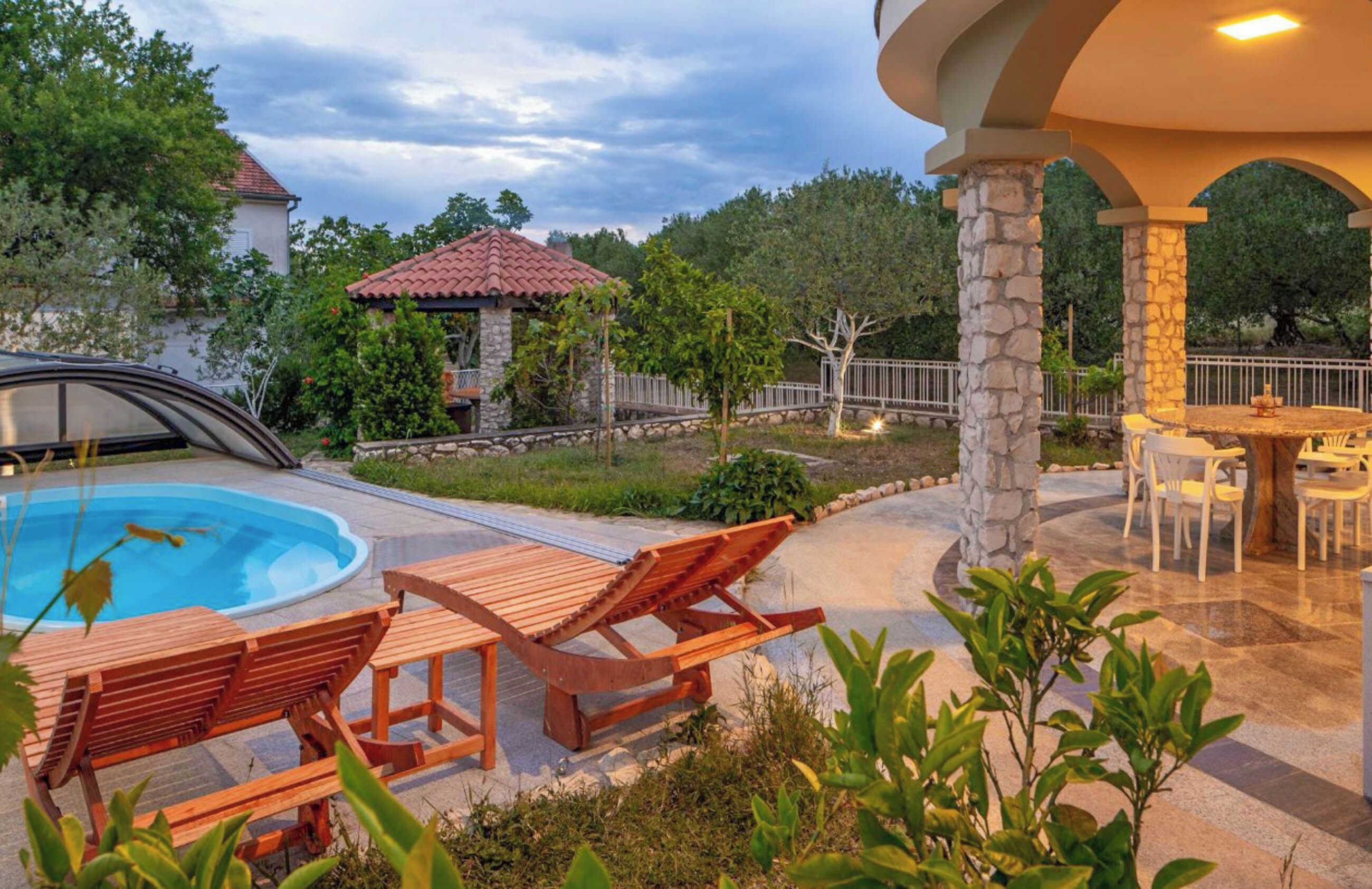 A pool area with wooden loungers, a gazebo, and a stone pillar.