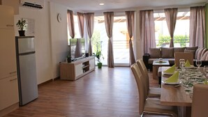 A modern kitchen with a refrigerator, a wooden dining table set for two, and a sofa in the background. - Villa Divine (Vodice)