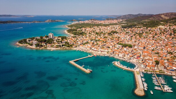 An aerial view of a coastal town with a marina, clear blue waters, and a mix of residential and commercial buildings. - Villa Divine (Vodice)