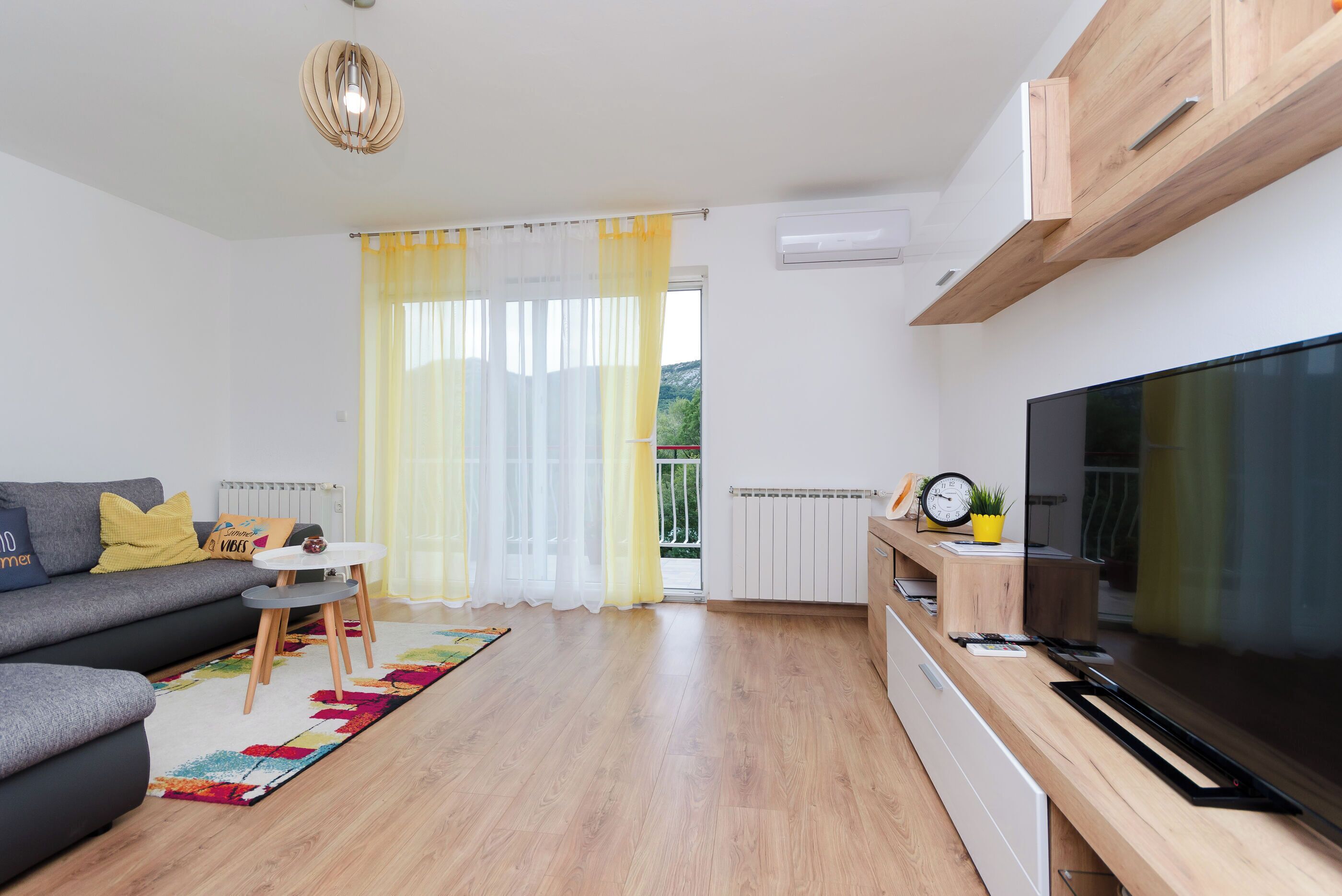 A modern living room with a sofa, a small table, a TV, and a window with curtains.