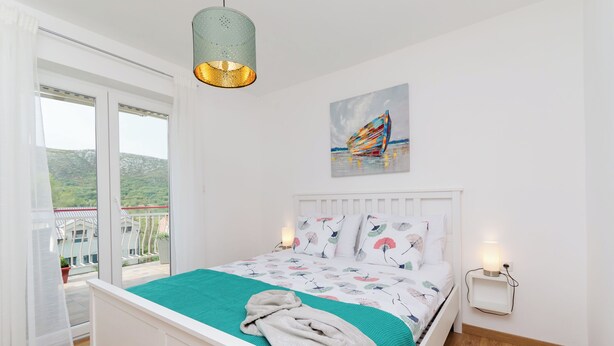A bedroom with a bed, a window with a view of greenery, a painting on the wall, and a bedside lamp. - Apartment Ivona (Vinodol)